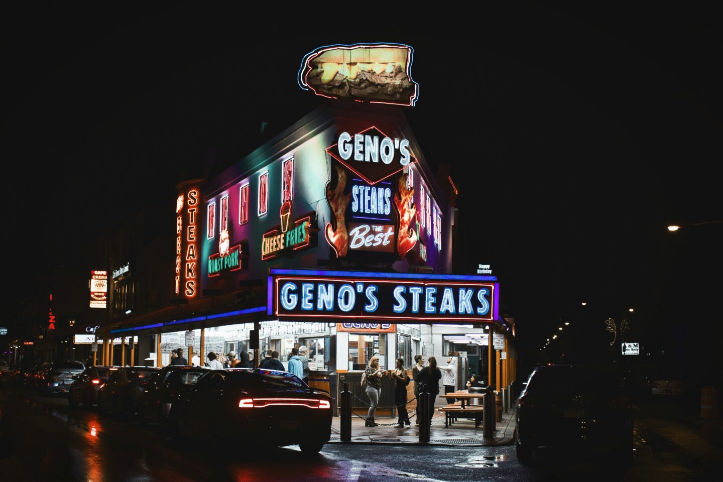 Neon lights of Philadelphia's Famous 'Geno's Steaks' at Night with People Eating Outside