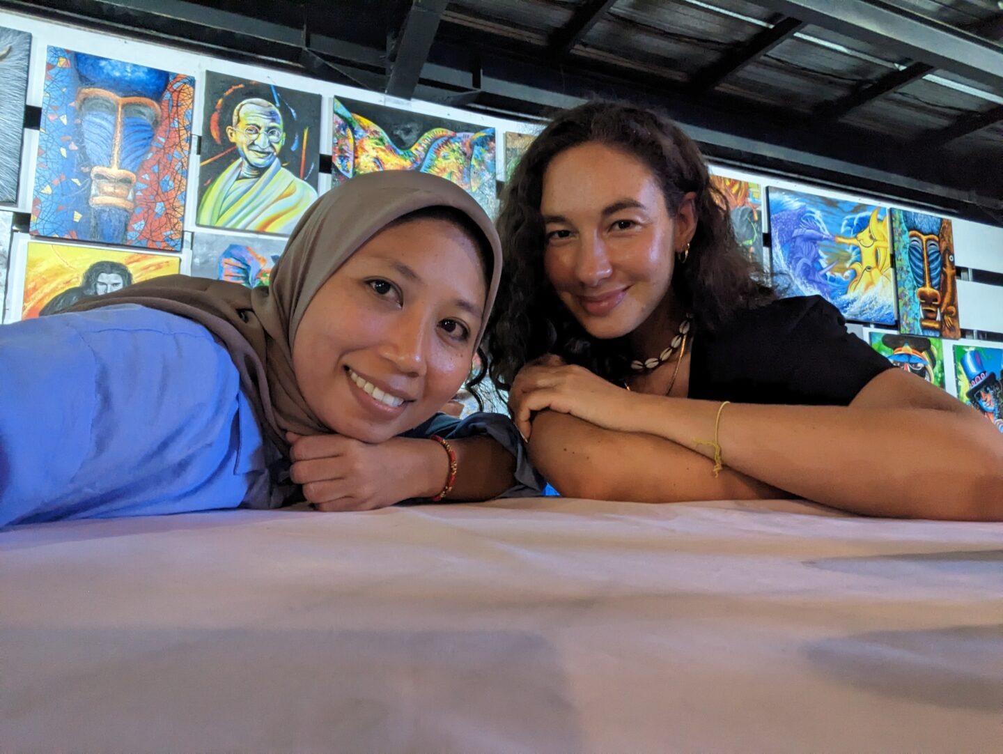Two smiling friends posing at an art gallery, with colourful paintings visible on the wall behind them, capturing a moment of joy and connection.