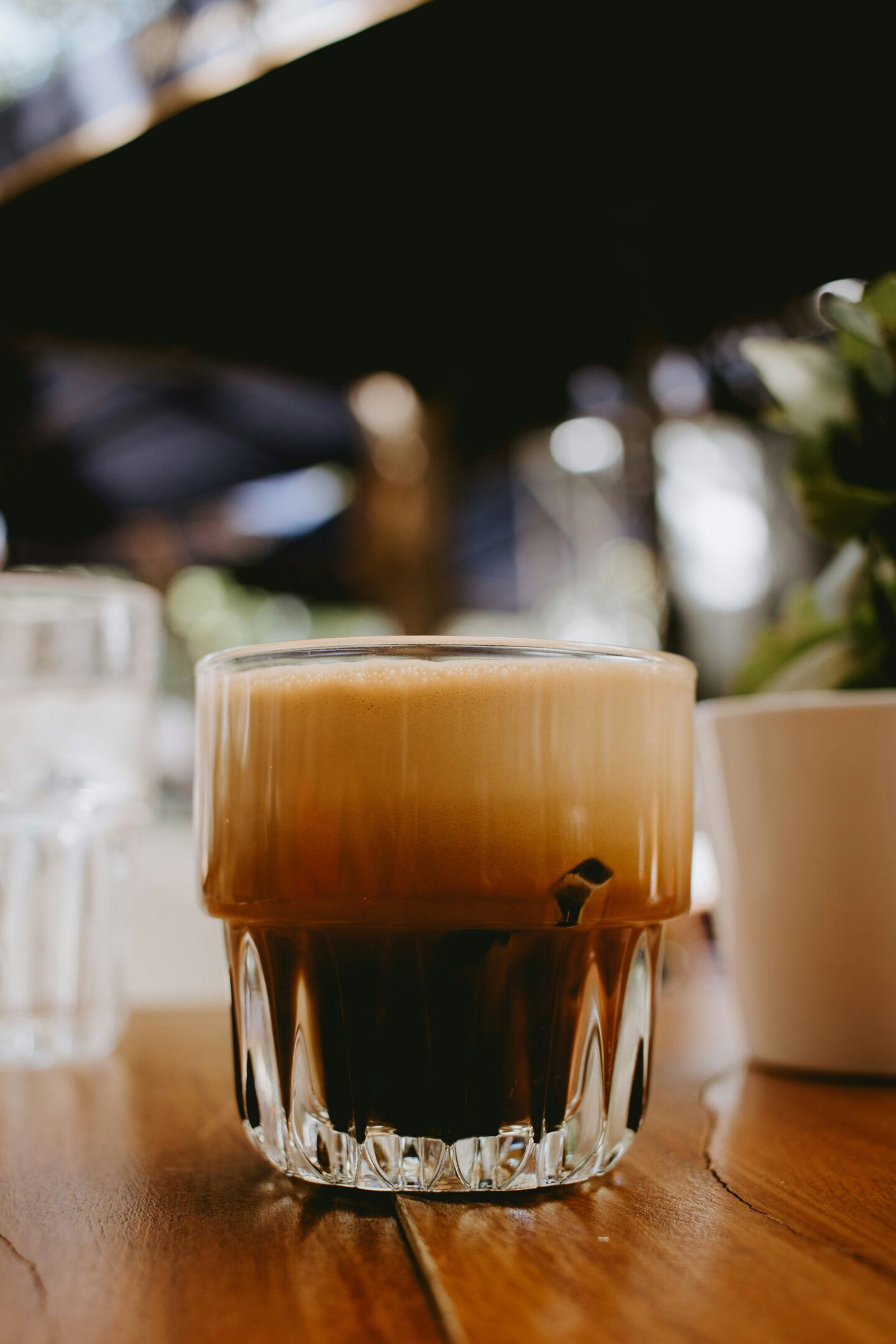 Image of Greek coffee: A close-up shot of a frothy glass of espresso freddo, sitting on a wooden table, with the foam and dark coffee layers visible, in a café in Athens.