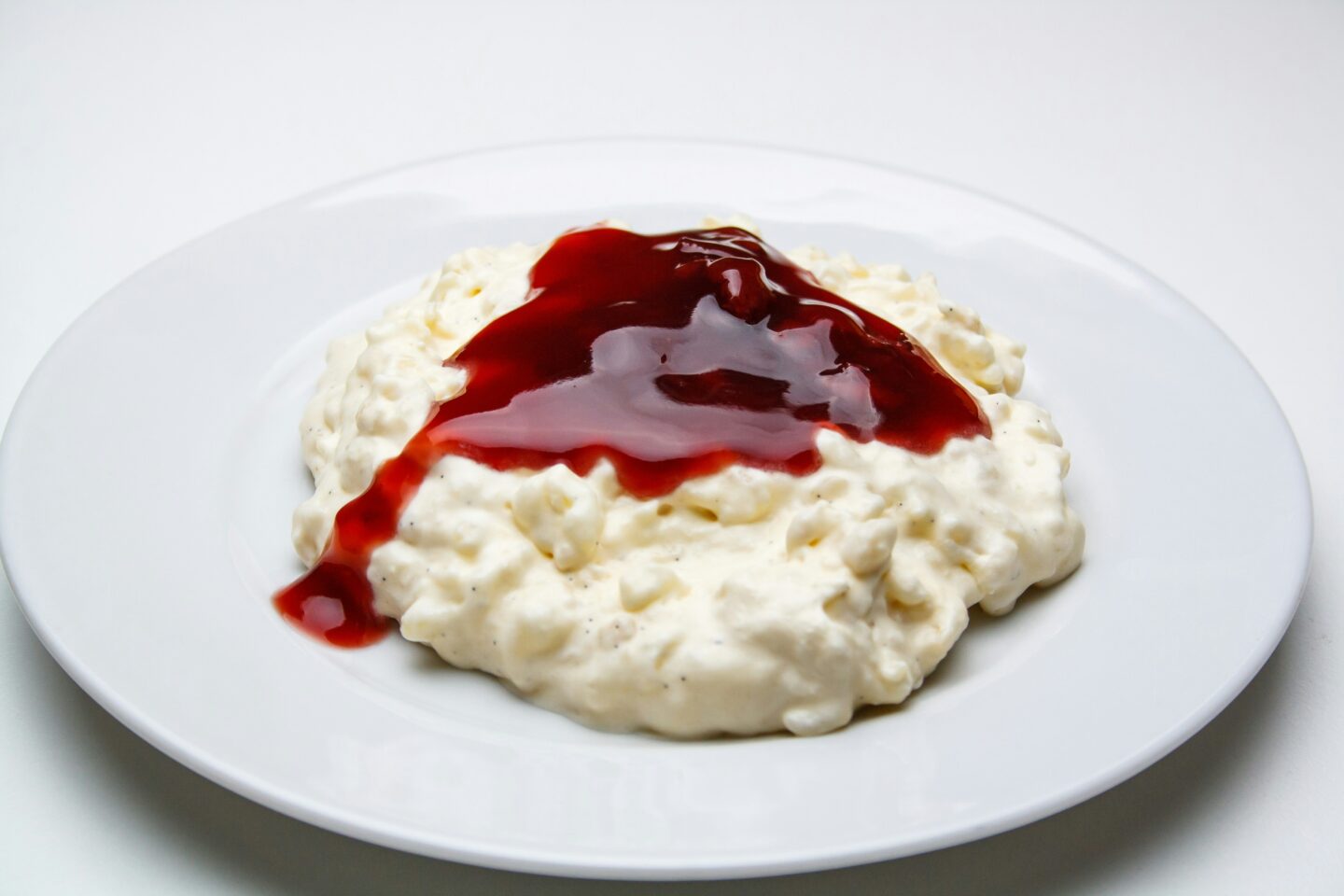 A plate of risalamande, a creamy Danish rice pudding topped with a generous swirl of red cherry sauce, served on a white plate, representing a traditional Danish Christmas dessert.