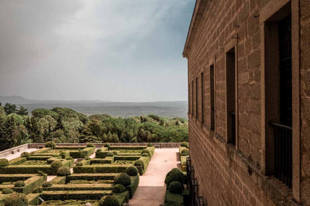 Scenic view of manicured gardens and a two-story stone building in San Lorenzo de El Escorial.