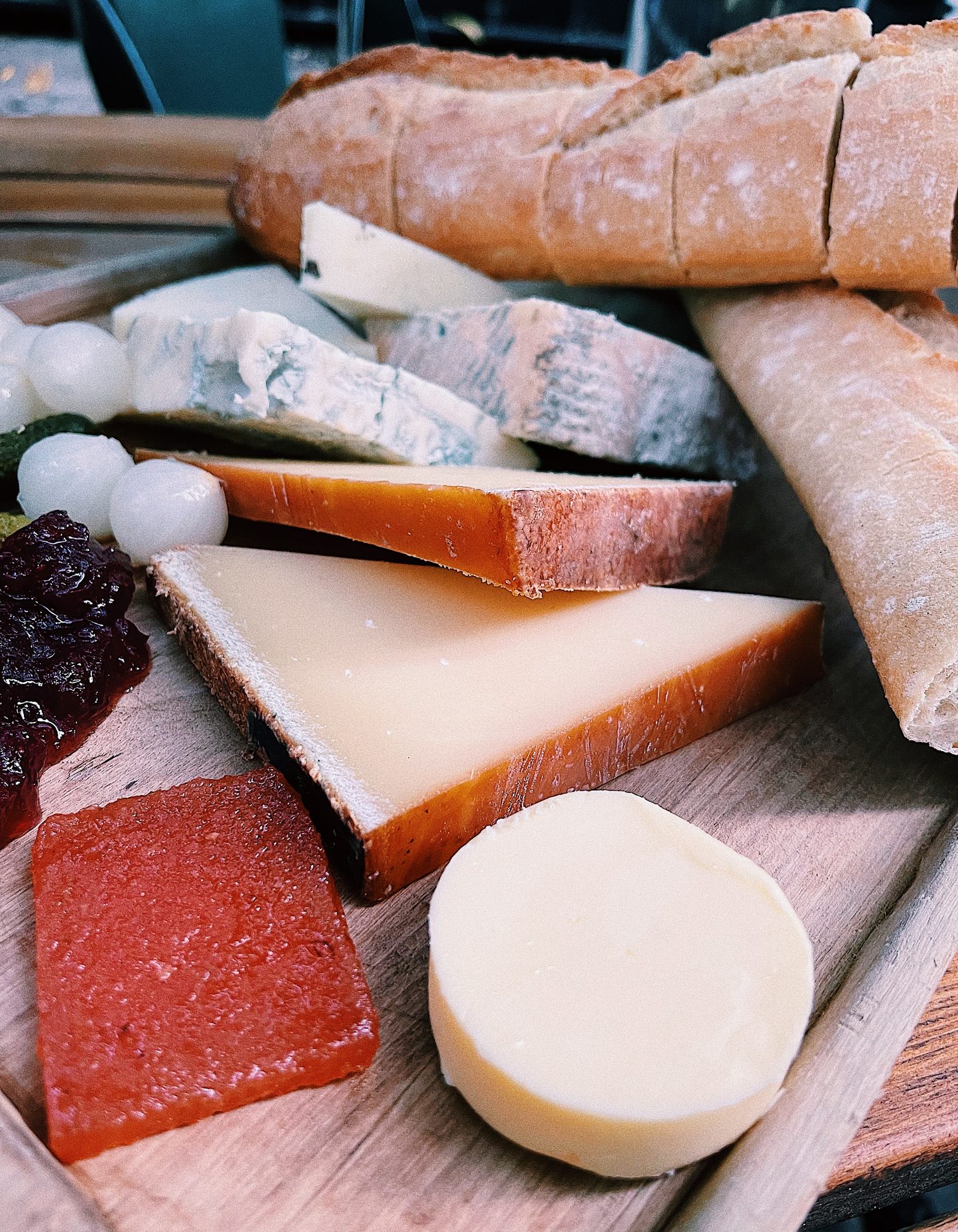 Close up of a cheese board at Gordons Wine Bar with wedges of hard and blue cheese soft cheese crusty baguette pickled onions cornichons chutney and quince paste. The generous sharing board pairs with wine at one of Londons historic wine bars.