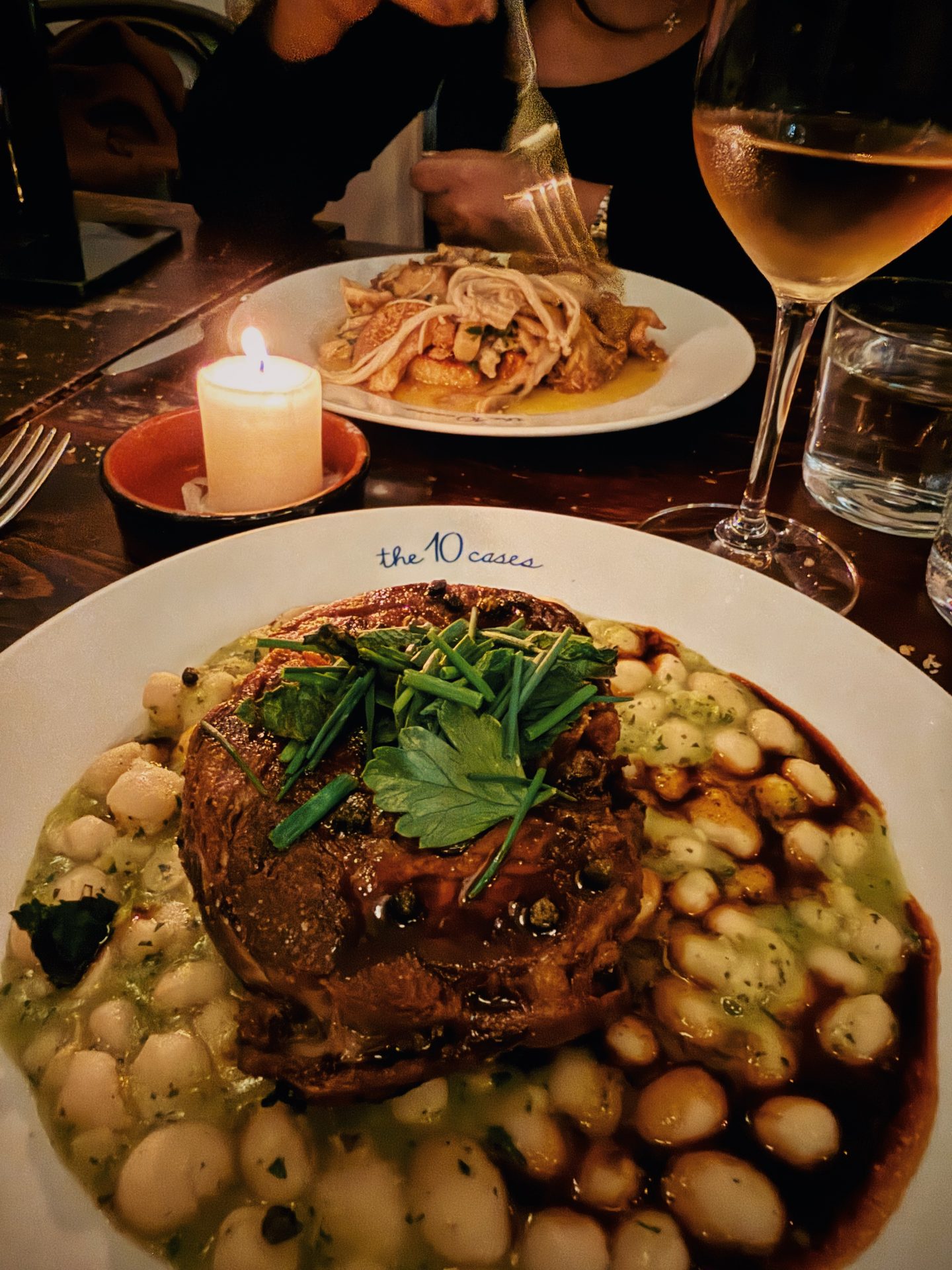 Candlelit dinner at The 10 Cases in Covent Garden with a hearty main of lamb white beans herbs and rich sauce alongside another shared plate. A glass of wine completes the cozy London wine bar setting.