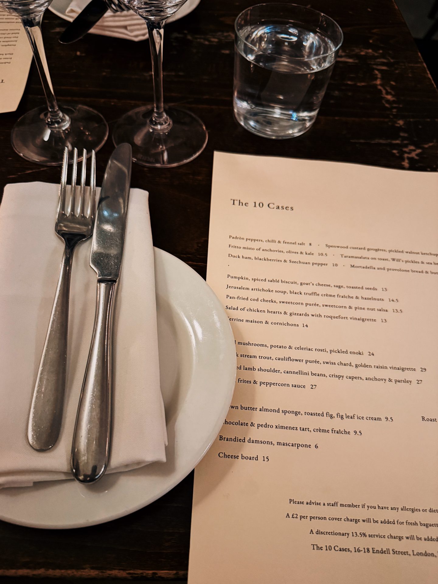 Table setting and menu at The 10 Cases in Covent Garden surrounded by wine glasses cutlery and a glass of water.